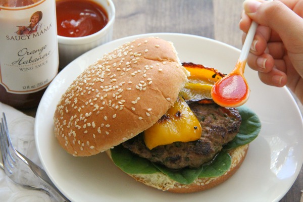 Burger in a bun with habanero sauce on a white spoon about to be drizzled on