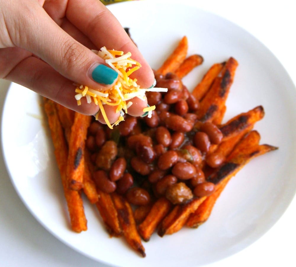 Hand sprinkling cheese on Chili Cheese Sweet Potato Fries on ShockinglyDelicious.com