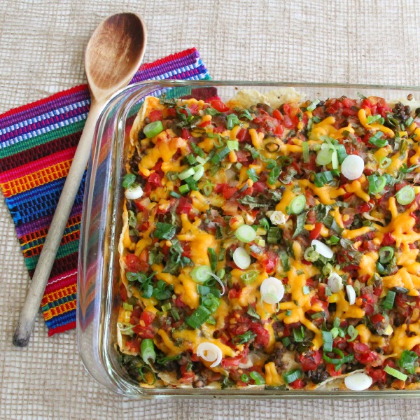Baked Lentil Chilaquiles Casserole in a glass baking dish with a woodenspoon and colorful napkin alongside