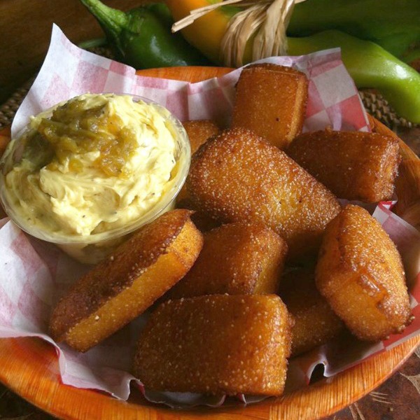 A basket of brown cornbread hush puppies with a ramekin of light yellow Hatch Chile Garlicky Butter on Shockinglydelicious.com