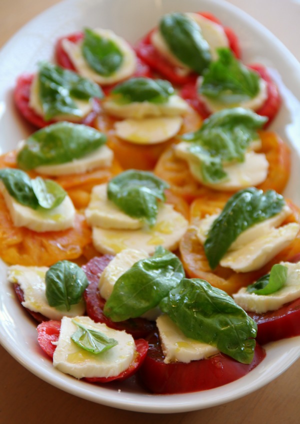 Heirloom tomatoes topped with fresh Mozzarella and basil leaves on a white platter.