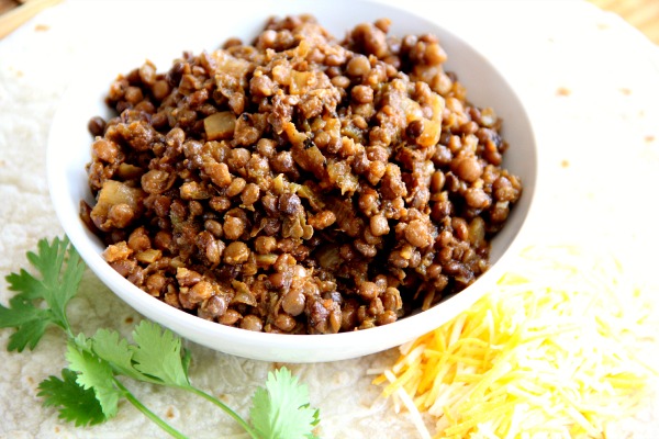 Triple Hatch Chile Lentil Tacos in a white bowl with cilantro and cheese surrounding it