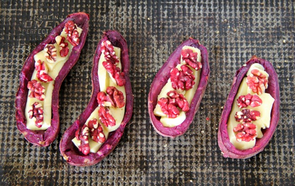 Hollowed out Purple Sweet Potato Skins stuffed with bried and topped with red walnuts on a gray baking sheet