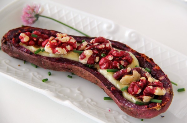 A Purple Sweet Potato Skin with Brie and Sweet Walnuts with a chive flower alongside on a white textured plate | Shockingly Delicious