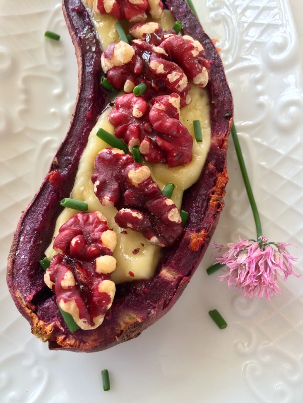 A Purple Sweet Potato Skin stuffed with Brie and topped with Sweet Walnuts on a white textured plate with a chive flower alongside | Shockingly Delicious