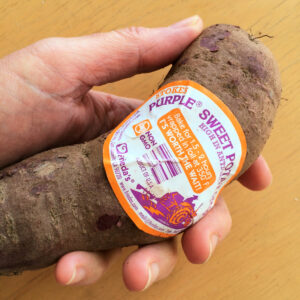 Stokes Purple Sweet Potato in a hand against a light wood background