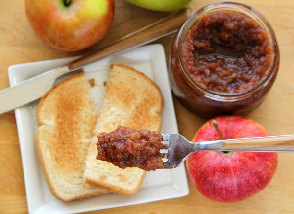 Slow Cooker Apple Butter on a fork in foreground, with toast, apples and jar of apple butter in background out of focus Recipe | ShockinglyDelicious.com