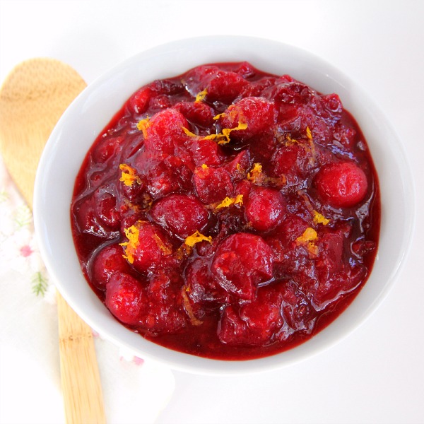 Dreamsicle Vanilla-Orange Cranberry Sauce in a white bowl on a white background with a wooden spoon alongside
