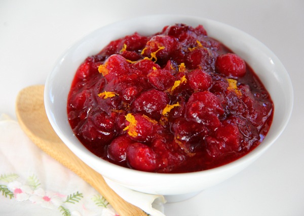 Bright red Dreamsicle Vanilla-Orange Cranberry Sauce with orange zest flecks and a wooden spoon alongside
