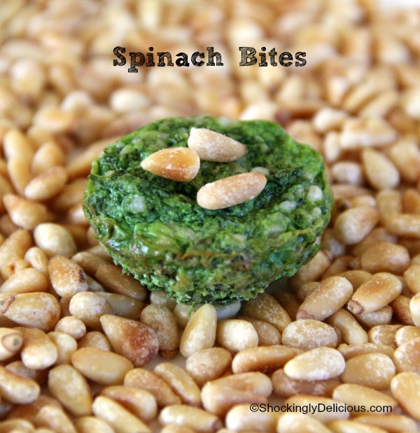 Small green Spinach Bites appetizer sitting on a bed of toasted pine nuts with words above it