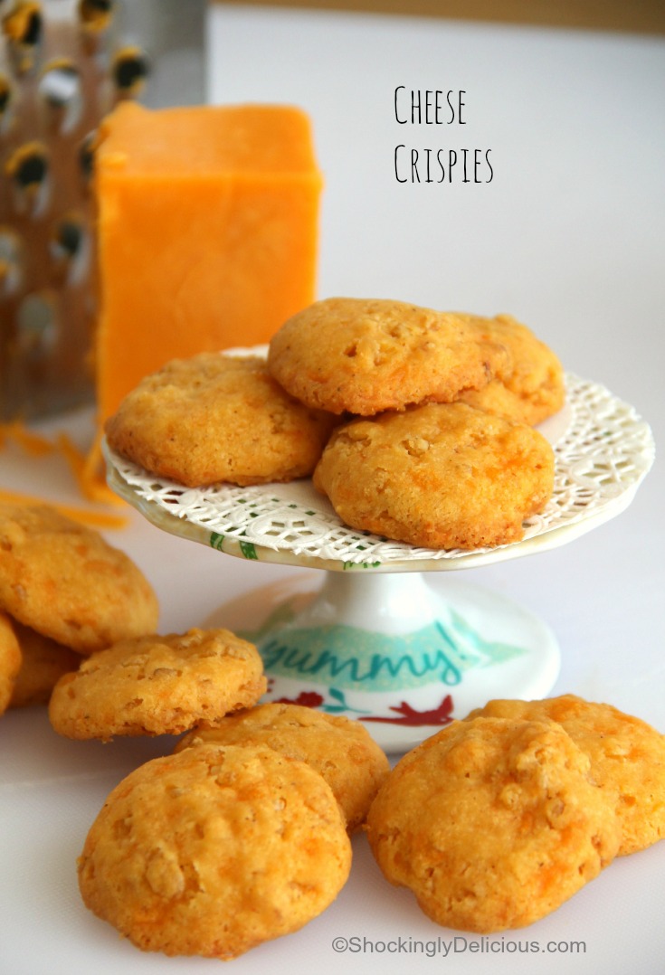 Cheese Crispies on a cake stand with cheese and a grater behind