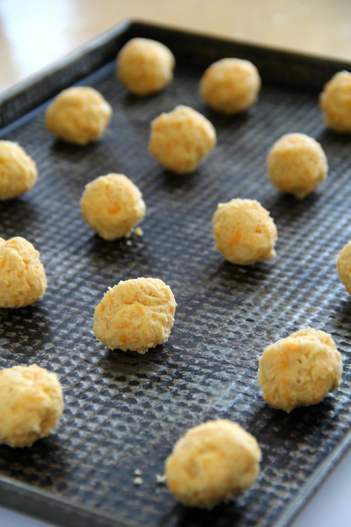 Dark cookie sheet full of cheese balls ready for the oven