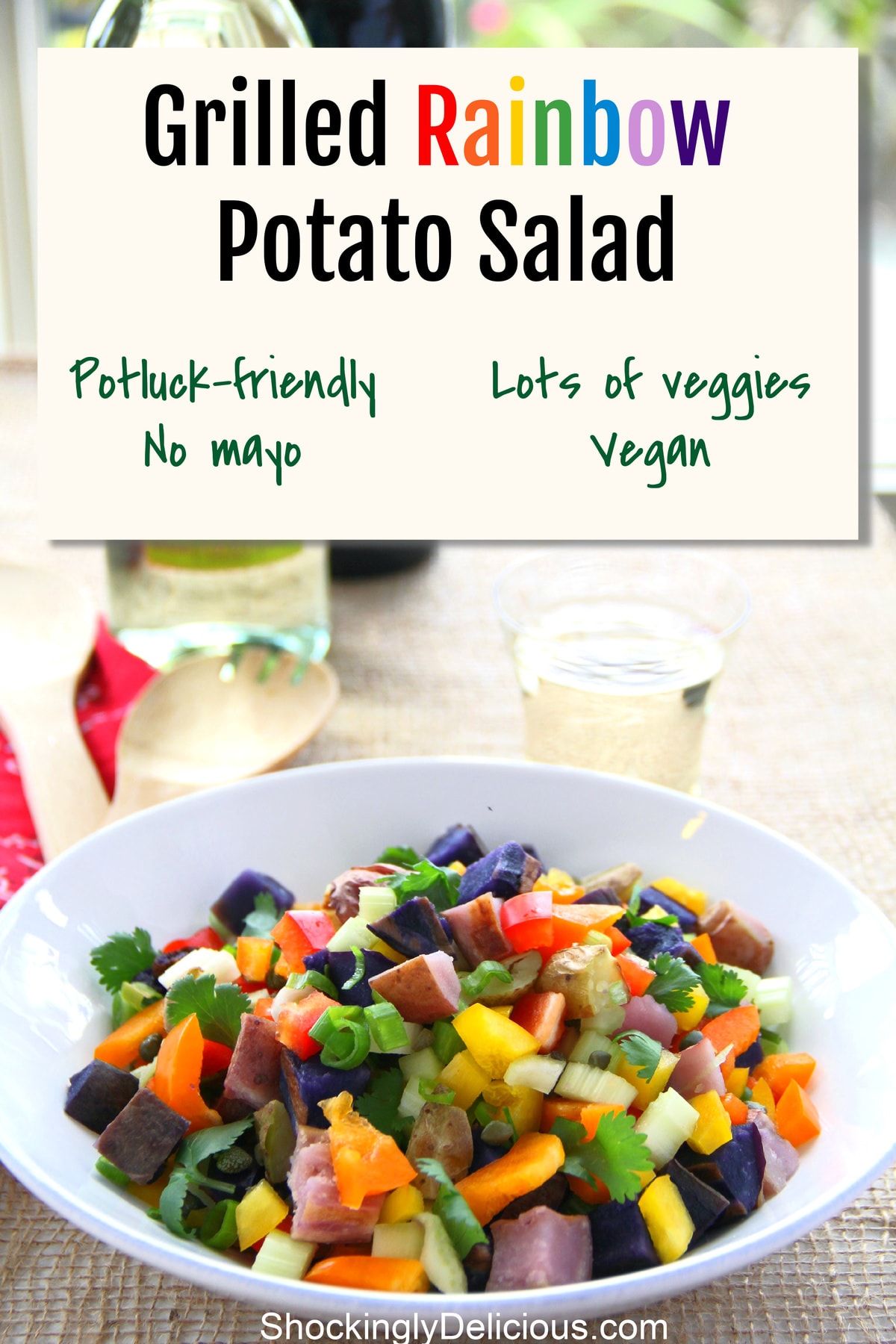 Grilled Rainbow Potato Salad in a white bowl on a burlap map with a wine glass behind it and the recipe title above it