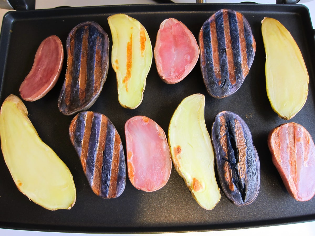 Purple, red and white fingerling potatoes on a black panini grill with grill marks on them