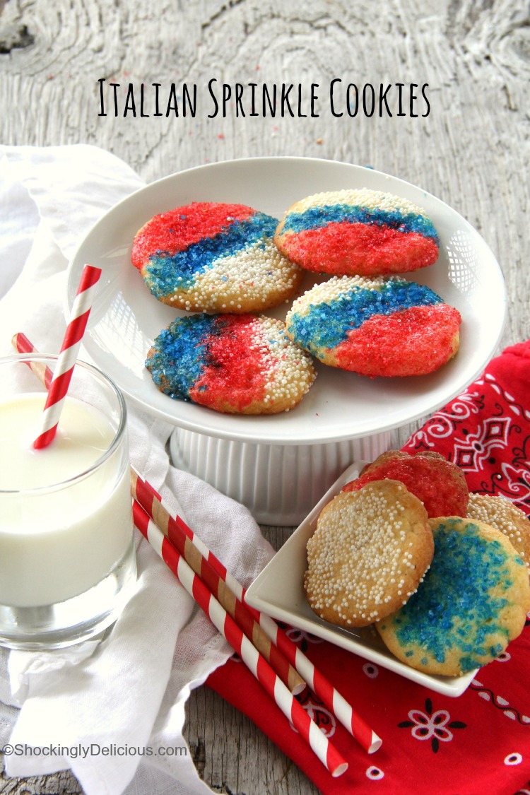 4 Italian Sprinkle Cookies with red white and blue sprinkles on an elevated white cake stand with a glass of milk to the sidedings, easy recipe | ShockinglyDelicious.com