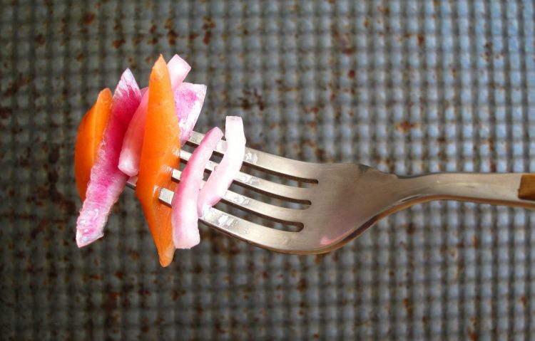 Orange carrot and purple onion slices alternating on the tines of a fork against a grey textured background
