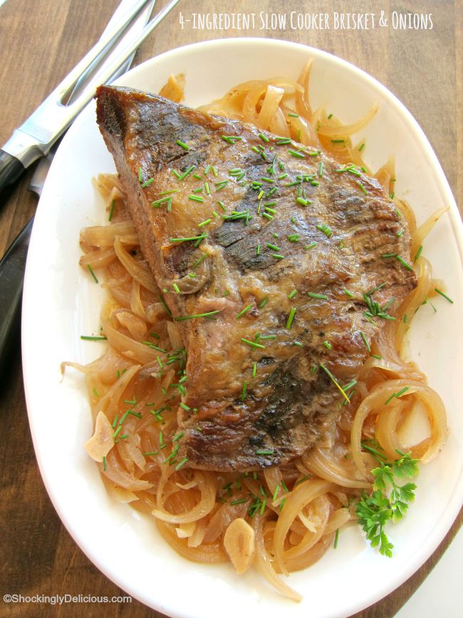 Cooked beef brisket atop a pile of cooked onions sits on a white platter on a wooden table, with carving utensils alongside is easiest, simplest, meltingly tender, for comfort food dinners | ShockinglyDelicious.com