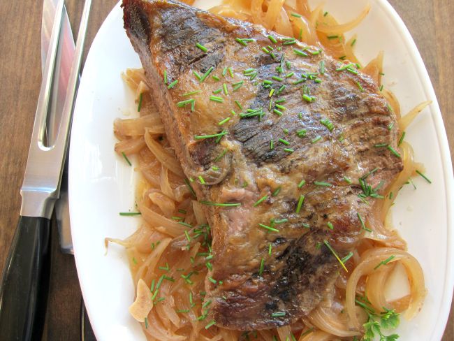 4-ingredient Slow Cooker Brisket with Onions on a white platter with carving utensils alongside