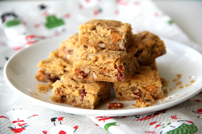 Butterscotch Pecan Shortbread stacked on a white plate with a holiday tea towel underneath