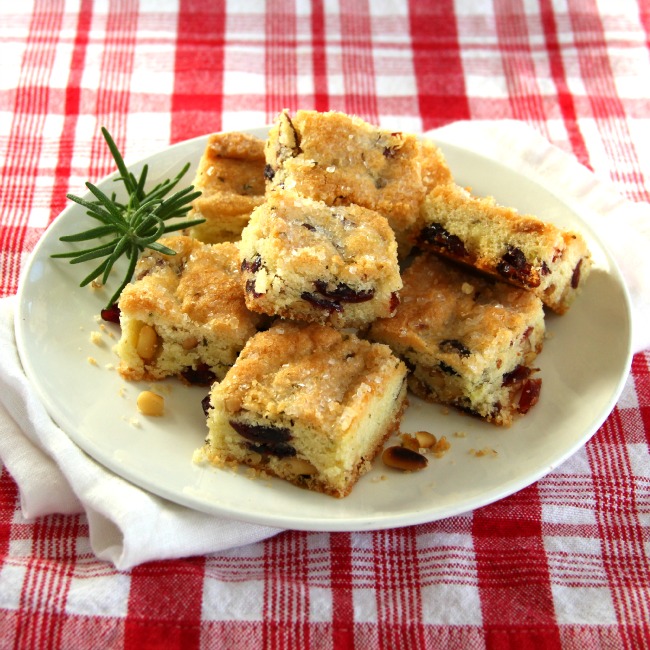 Cranberry Rosemary Shortbread stacked on a white plate with a red plaid tablecloth underneathelicious.com