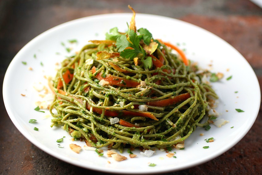 Edamame Spaghetti with Kale Cilantro Pesto piled on a white plate set on a brown tabletop on ShockinglyDelicious.com