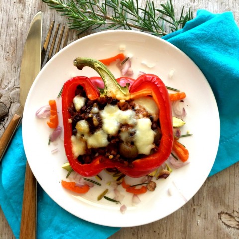 Red pepper stuffed with vegetarian picadillo on a white plate, with a blue napkin underneath and rosemary sprig on the table. 