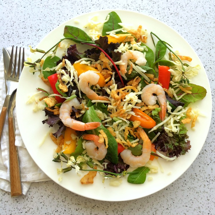 Salad with greens and shrimp on a white plate with fork on the left