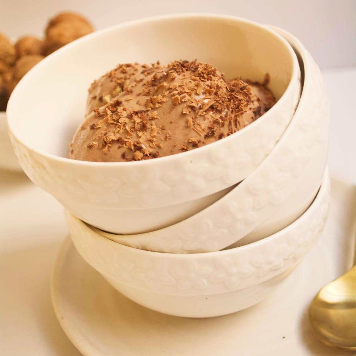 Scoops of milk chocolate ice cream in cream-colored stacked bowls.