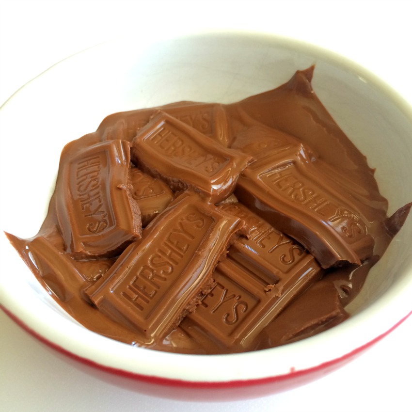 Partially Melted Hershey Bars in a white bowl with a red exterior. 