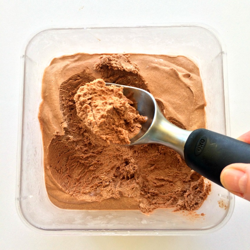 Black handled ice cream scoop digs out Milk Chocolate Ice Cream from a square plastic container.
