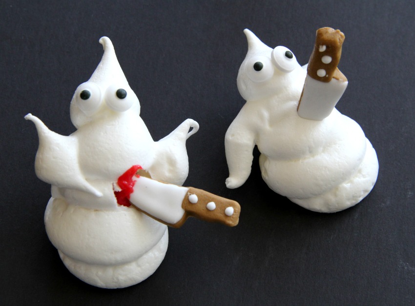 2 candy decoration knives stuck into 2 white ghost meringue cookies against a black backgrounds-com