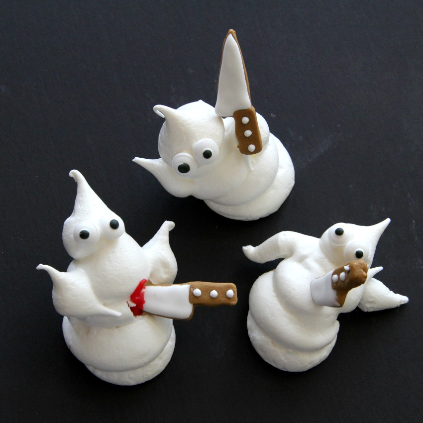 3 white ghost meringue cookies and 3 candy knives against a black background on ShockinglyDelicious.com