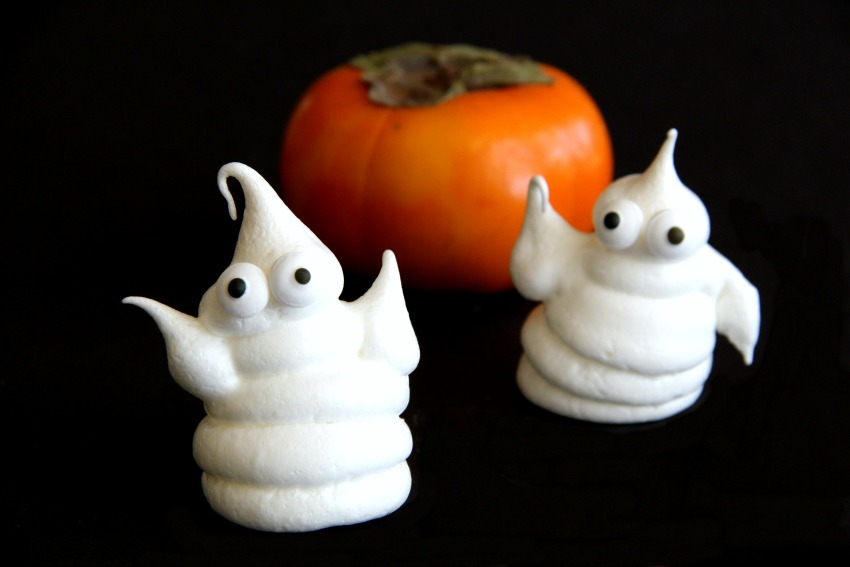 2 Halloween Ghost Cookies with an orange persimmon behind them. 