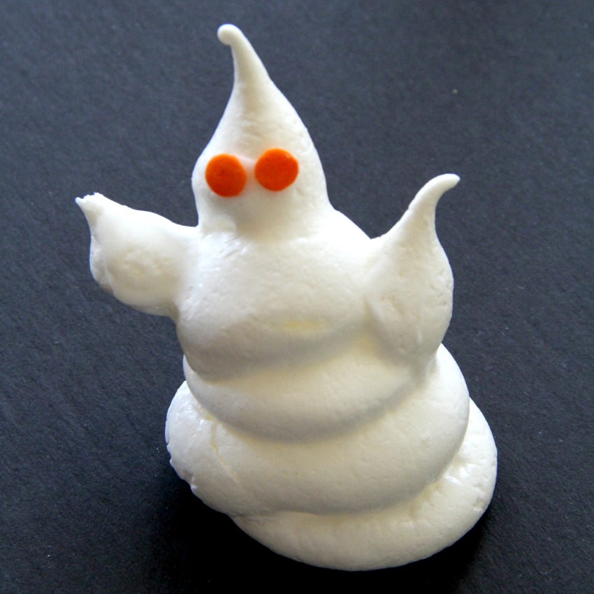Halloween Ghost Meringue Cookie with orange eyes against a black background on ShockinglyDelicious.comlydelicious-com
