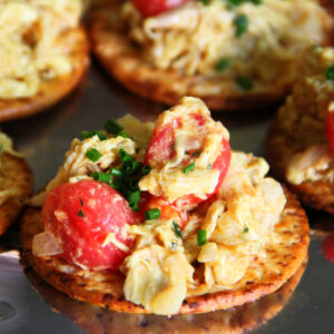 Coronation Turkey Salad piled onto a cracker with cherry tomatoes on top on ShockinglyDelicious.com
