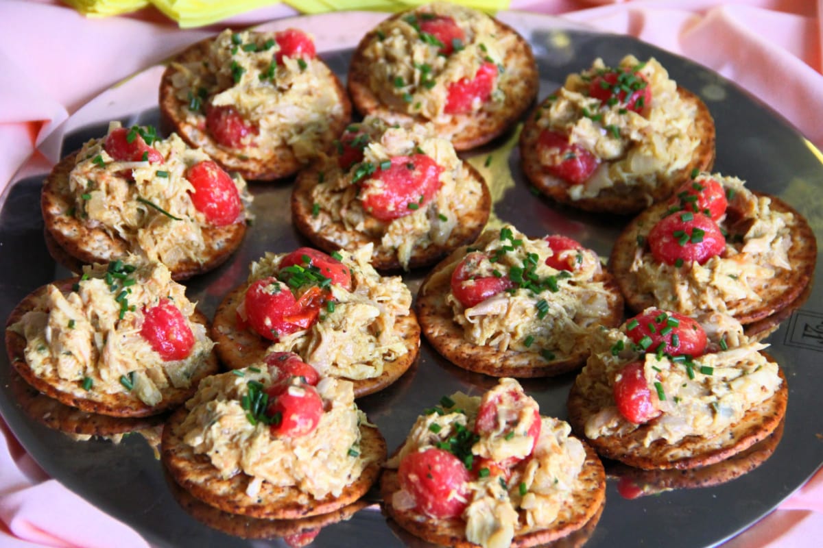 A tray of crackers topped with Coronation Turkey Salad with cherry tomatoes on top 