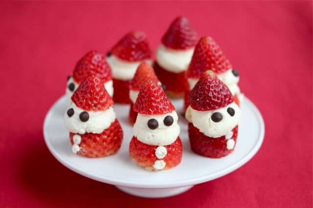 santa-shaped strawberries on a white cake plate with a red background