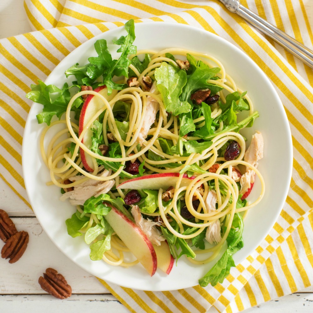 Apple and Arugula Pasta with Chicken on a white plate with striped yellow cloth underneath