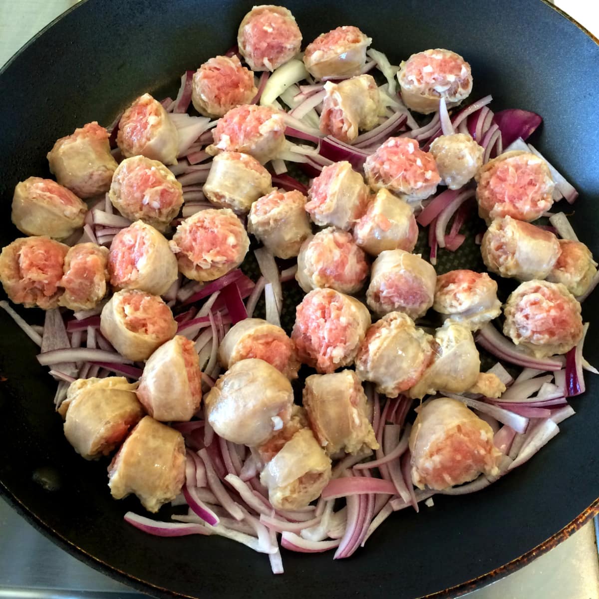 Sausage and purple onion slices cooking in a black skillet 