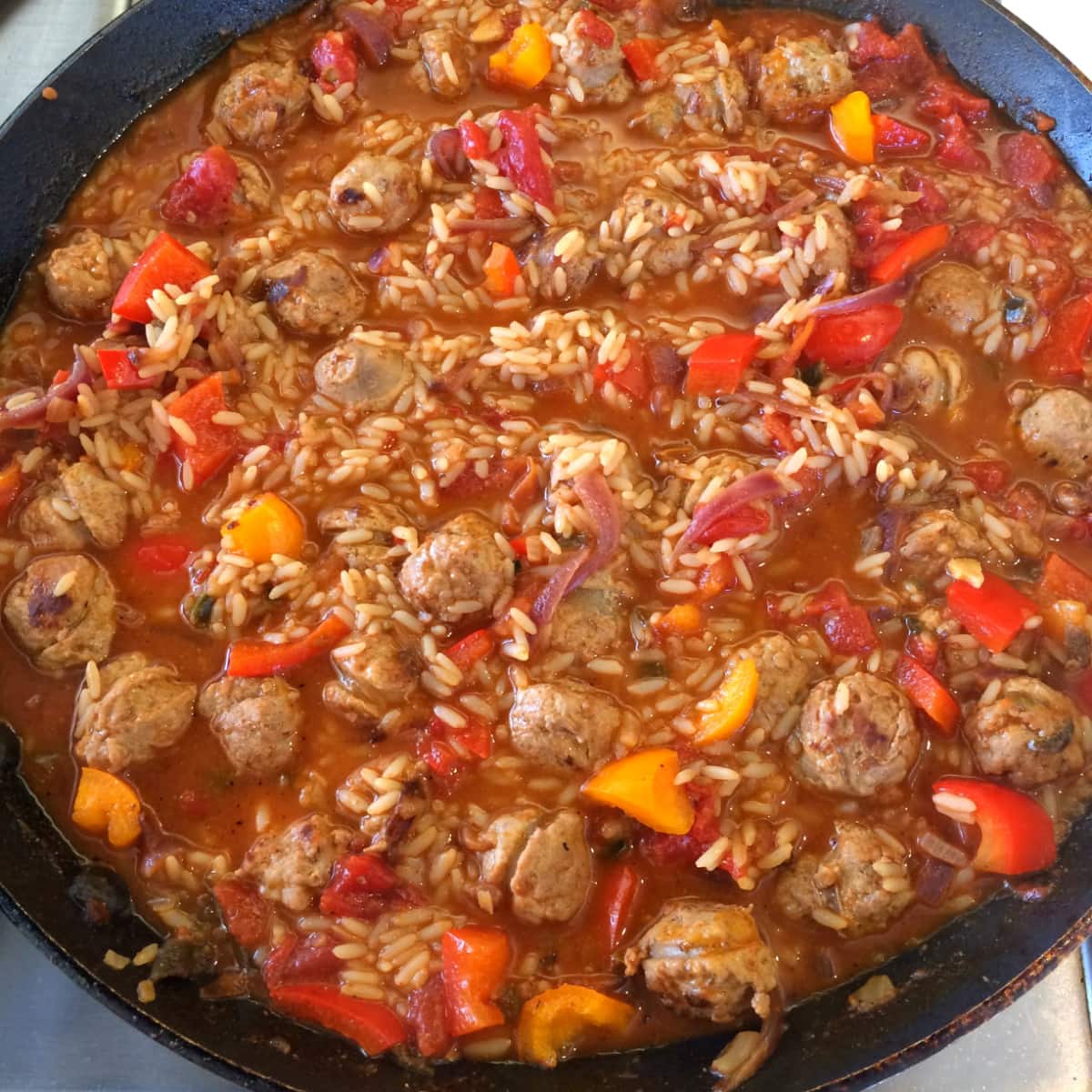 Peppers are stirred into Hawaiian Jambalaya Skillet in a black skillet