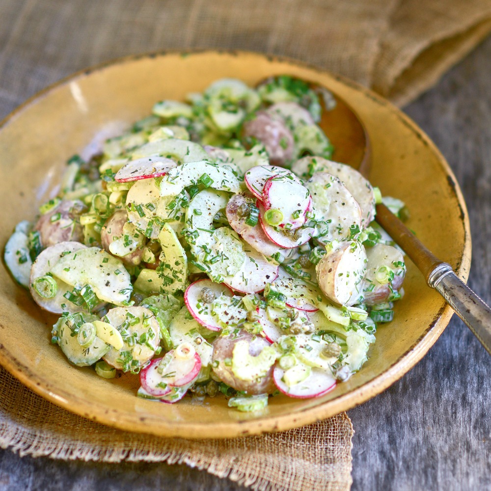 Grandmother Ida's Russian Potato Salad in a yellow bowl on a wooden table