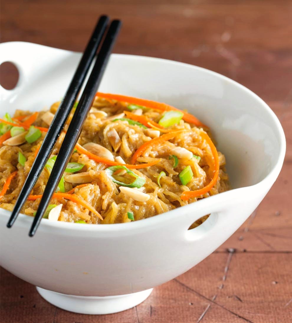 Noodles with carrot shreds and chopped onions in a white bowl with chopsticks set on top