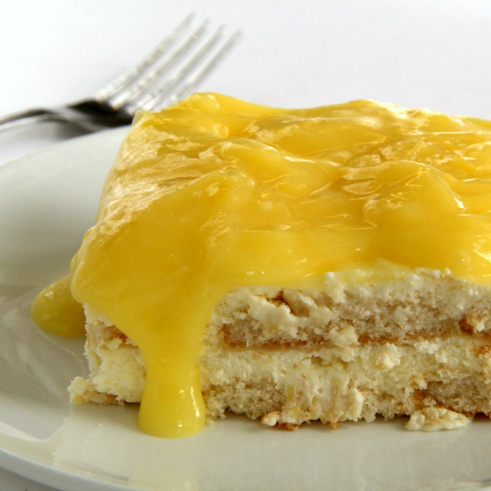 A layered square piece of Lemon Icebox Cake with a thick layer of lemon curd on top and a fork in the background