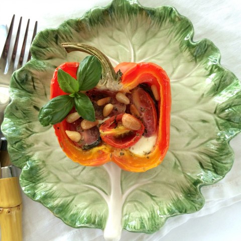 Striped bell peppers stuffed with caprese ingredients on a green ceramic lettuce plate with bambook silverware beside it.  Stuffed Pepper on ShockinglyDelicious.com