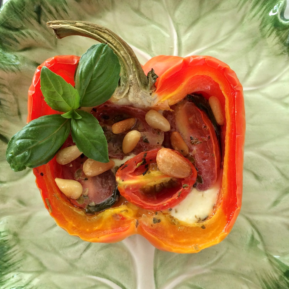 Half a red pepper stuffed with caprese salad ingredients on a green leaf plate