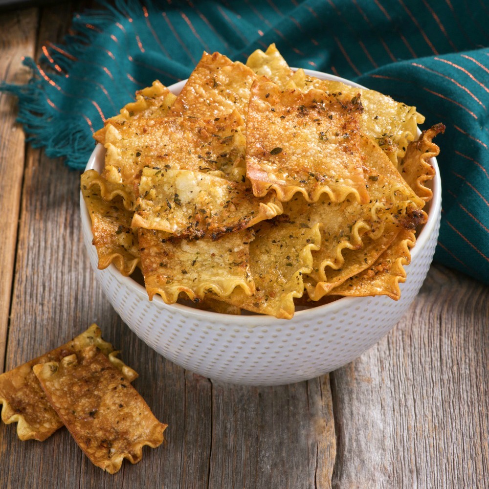 Crispy brown Oven-Baked Herbed Lasagna Chips in a white bowl on a wooden table on ShockinglyDelicious.com