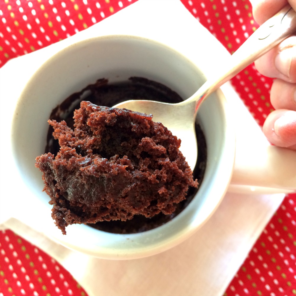 Spoon digging into Mug brownie with red wine in a white cup on a red patterned towel
