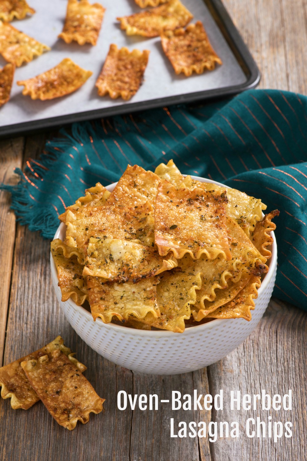 Oven-Baked Herbed Lasagna Chips recipe name superimposed atop a photo of brown lasagna noodle chips in a white bowl, with a cookie sheet of the chips in the backgrounda Chips on a baking sheet and in a white bowl on ShockinglyDelicious.com