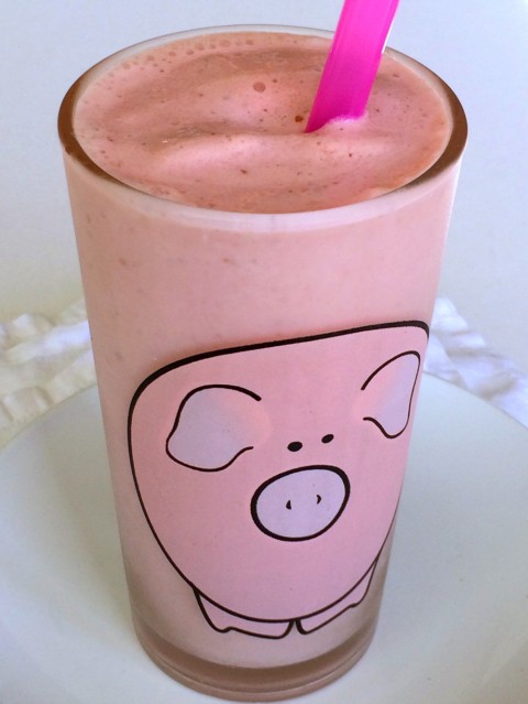 Pink colored Pineapple Blood Orange Smoothie in a glass decorated with a pig, on ShockinglyDelicious.com