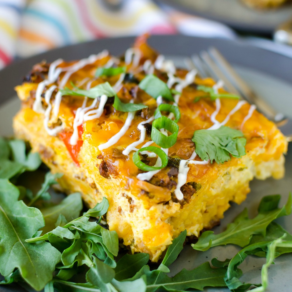 Square piece of yellow-colored Overnight Mexican Breakfast Casserole on a bed of arugula with sliced green onions on top